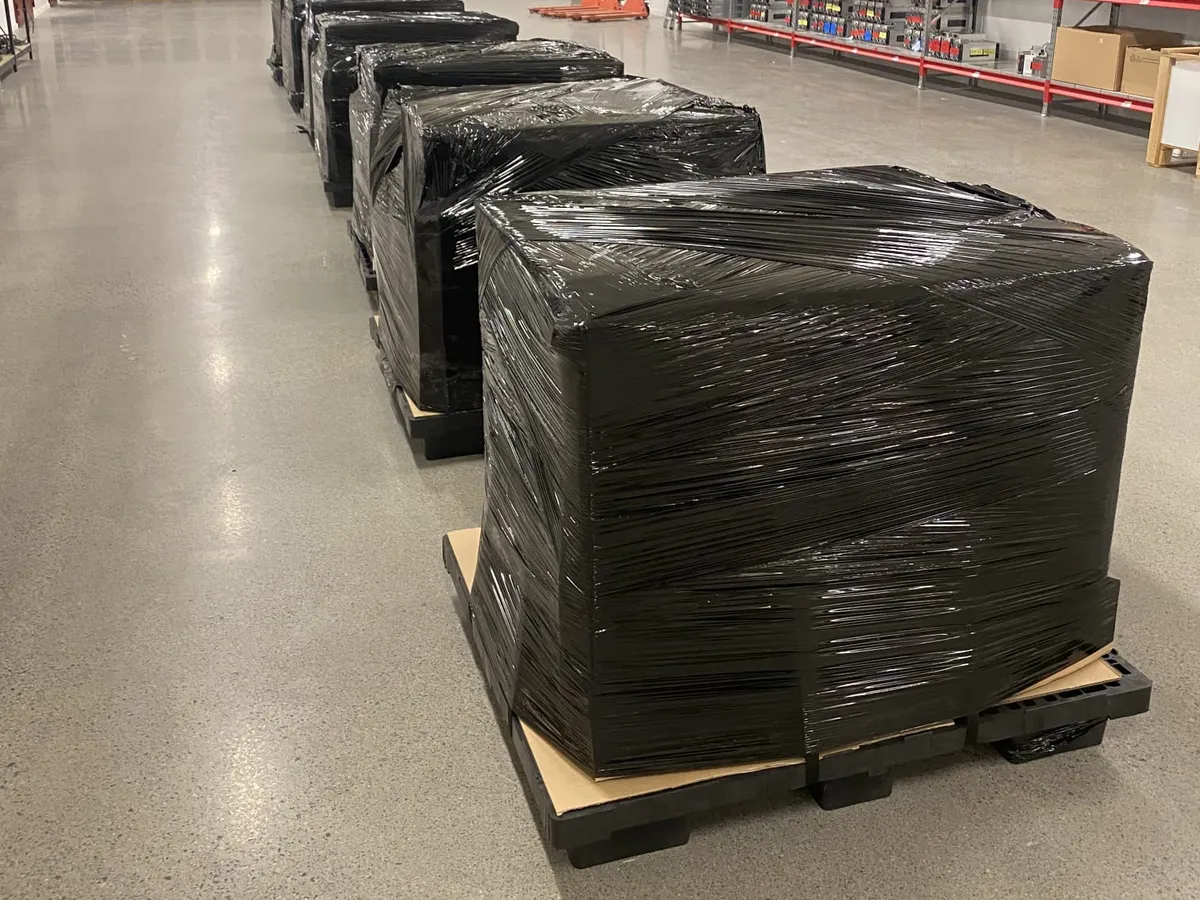 A row of pallets wrapped in black stretch film on a warehouse floor.