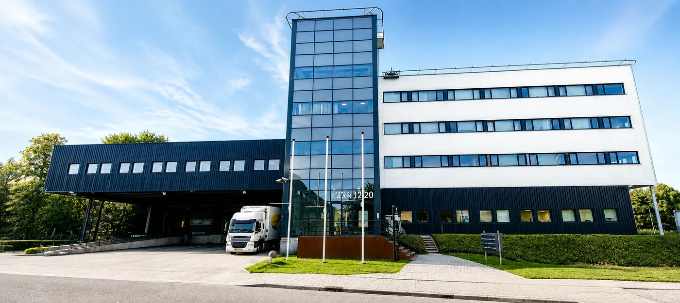 The office building at Capronilaan in Schiphol Rijk: a glass stair tower between a dark loading wing, with a truck at its dock, and a white four-storey block.