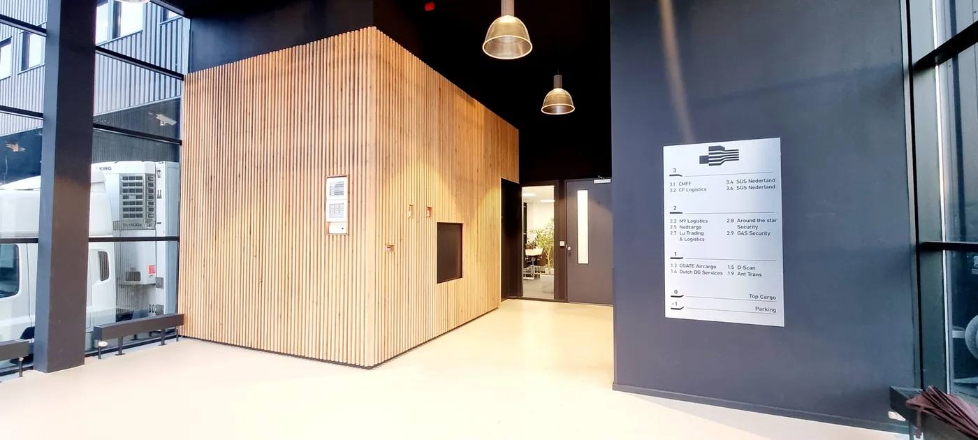 The ground-floor hall: a wall of wooden slats, pendant lamps, and the tenant board listing CF Logistics on the third floor.