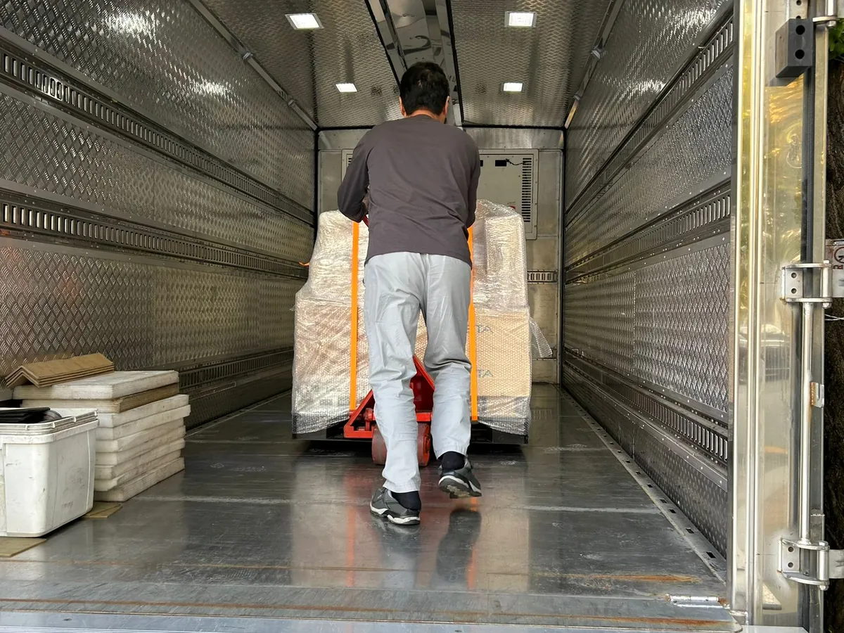 A man walking a pallet on a hand pallet truck into the box of a truck lined with aluminium panels.